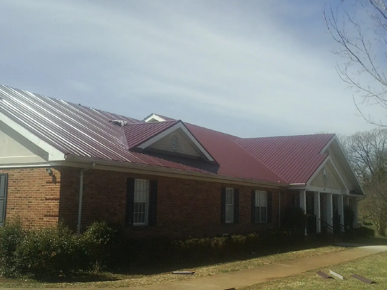 Red metal roof with gabled entries on a long brick building, from a Hail Damage Roof Repair job in Midland Park