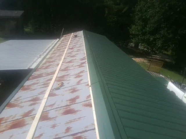 Old rusted panels beside newly installed green metal roofing — Wind Damage Roof Repair by Roofing Brothers in Midland Park