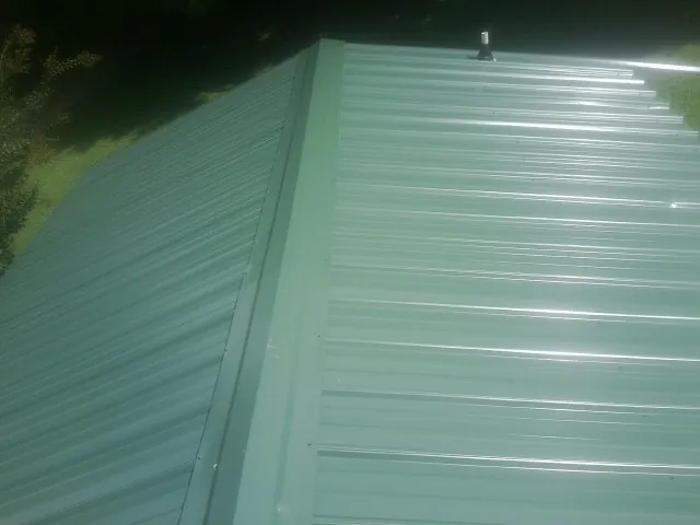 New green metal panels meeting at the ridge of a roof — Flat Roof Repair work by our crew in Midland Park