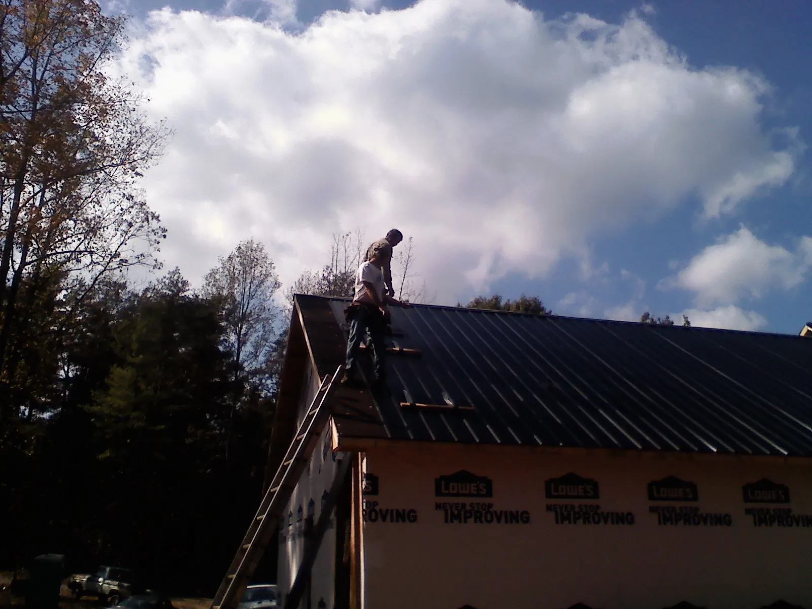 Roofer fastening dark metal panels high against a cloudy sky, from a Roof Inspection job in Midland Park