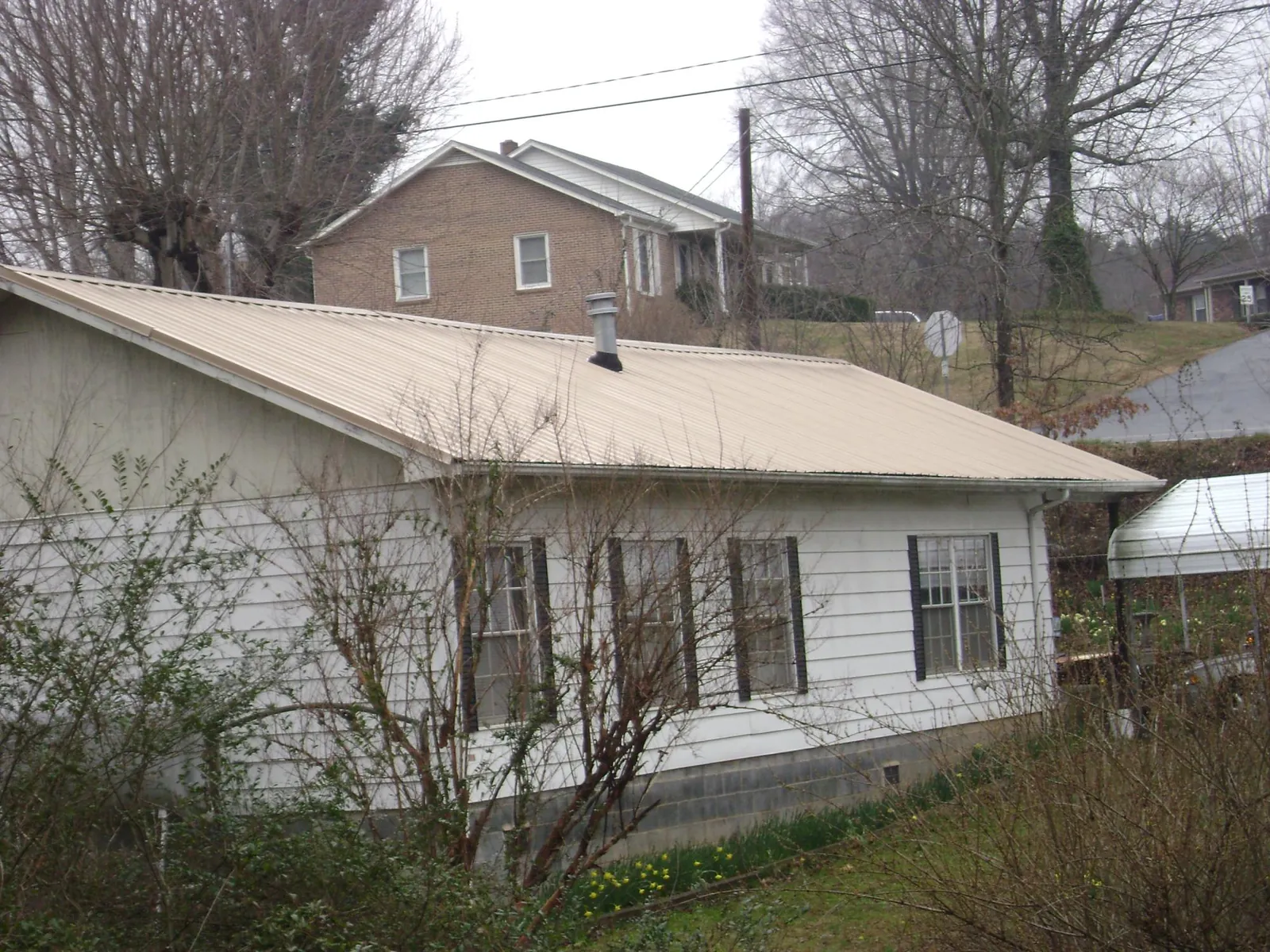 Tan metal roof on a white sided house set into a hillside — Commercial Roofing by Roofing Brothers in Midland Park